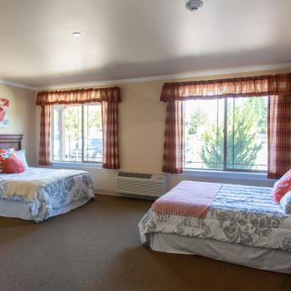 A spacious bedroom with two neatly made beds, large windows letting in natural light, and patterned curtains.