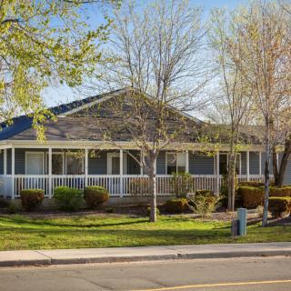 A picturesque suburban house with a spacious front porch and lush greenery on a sunny day.
