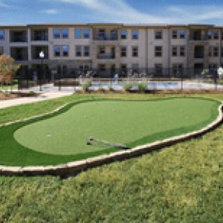 A neatly maintained putting green situated in front of a residential complex.