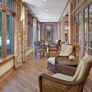 A cozy sunroom featuring rattan chairs and a wooden floor, with large windows offering ample natural light.