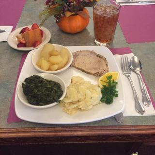 A plated meal with spinach, potatoes, meat, and a side of fruit.