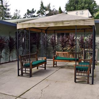 A cozy patio with a gazebo and wooden benches featuring green cushions.