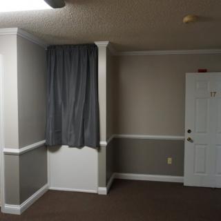A small empty room with gray walls, a door, and dark curtains.