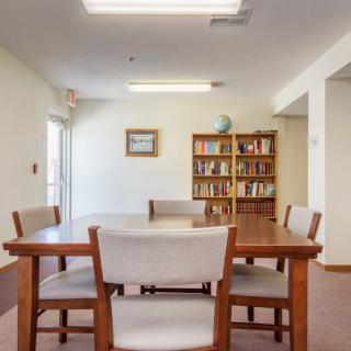 A modern meeting room with a wooden table, chairs, and a bookshelf filled with books.