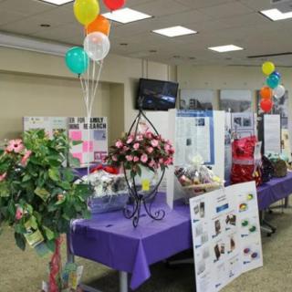 An indoor exhibition setup with colorful balloons, flowers, and informational displays on tables.