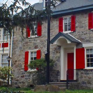 A charming stone house with red shutters and a sloped roof.