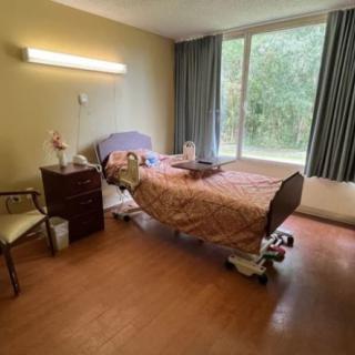 A hospital room with a single bed, nightstand, and a chair by the window.