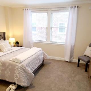 A cozy and well-decorated bedroom with a neatly made bed, soft lighting, and a window with white curtains.