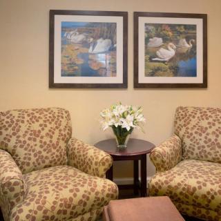 A cozy waiting room with patterned chairs, a small table with flowers, and framed artwork on the wall.