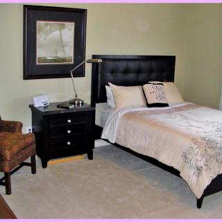 A neatly arranged bedroom with a bed, nightstand, chair, and artwork on the wall.