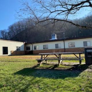 A sunny day highlights a picnic table in front of a small building surrounded by trees.
