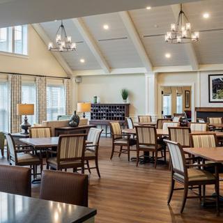 A spacious and well-lit dining room with multiple tables and chairs, elegant chandeliers, and large windows.
