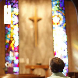 A person sits quietly in a church, reflecting amidst the colorful stained glass windows.