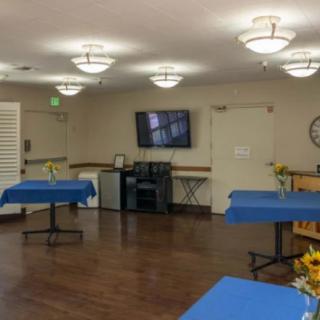 A community center room with tables covered in blue tablecloths and a wall-mounted television.