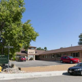 A small building with a parking lot, surrounded by trees on a sunny day.