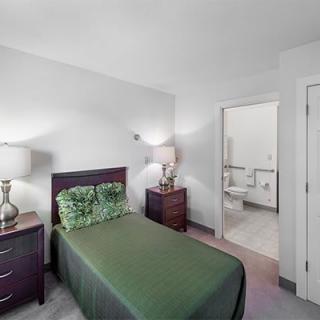A cozy bedroom with a single bed and green bedding, featuring a connected bathroom.