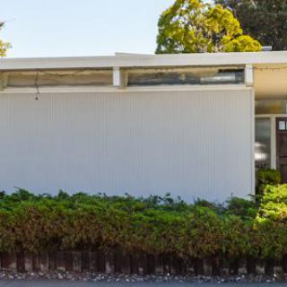 A minimalist modern building with a white facade and large windows, surrounded by greenery.