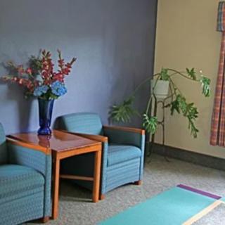 A waiting room with two chairs, a small table, a vase of flowers, and a potted plant.