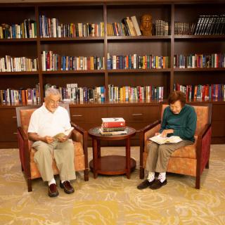 An elderly couple reading in a cozy library setting surrounded by books.