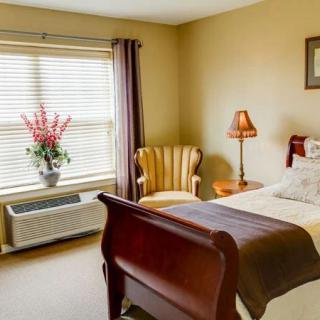 A cozy bedroom with a bed, an armchair, a lamp, and a window with curtains.