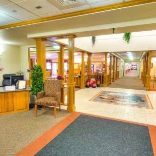 A brightly lit lobby area featuring wooden columns, seating, and a hallway leading further inside.