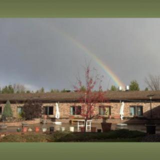 A rainbow arcs over a building with surrounding trees and a cloudy sky.