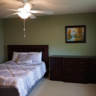 A cozy and well-decorated bedroom featuring a bed with a patterned blanket, a dresser, and a ceiling fan.