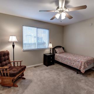 A cozy bedroom with a single bed, rocking chair, and lamp under a ceiling fan.