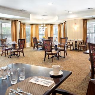 An elegant dining room with neatly arranged tables and chairs, featuring soft lighting and large windows with curtains.