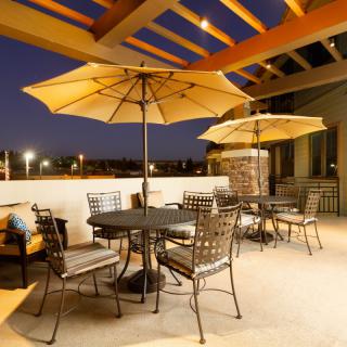A cozy outdoor patio area with tables and umbrellas, illuminated in the evening light.