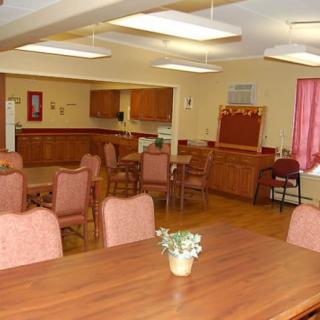 A communal dining area with several tables and chairs, featuring a small kitchenette in the background.