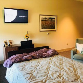 A cozy bedroom featuring a neatly made bed, a mounted television, artwork on the wall, and a comfortable chair.