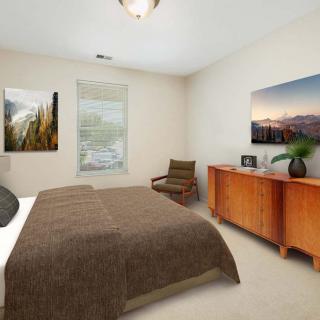 A cozy bedroom featuring a bed with a brown blanket, wooden dresser, artwork on the walls, and a window with natural light.