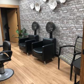 A modern salon interior with chairs and hair dryers against a brick wall backdrop.
