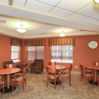 A cozy dining area with several tables and chairs, featuring soft lighting and a wall clock.