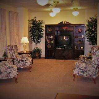 A cozy living room featuring floral-patterned chairs, a dark wooden television unit, and decorative plants.