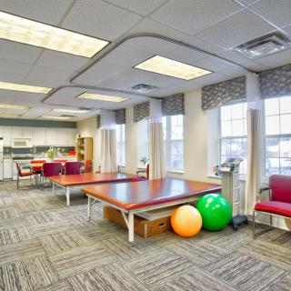 A bright and spacious physical therapy room equipped with tables, exercise balls, and chairs.