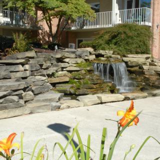 A small waterfall cascades over rocks in a landscaped garden, adorned with orange flowers.