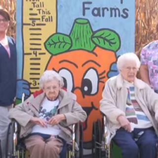 Elderly individuals enjoying a day at the farm with a cheerful carrot decoration in the background.