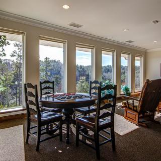 A cozy living room with large windows and a round table surrounded by chairs.
