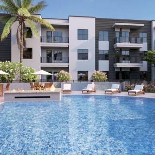 Modern apartment complex with a large swimming pool surrounded by sun loungers and palm trees.