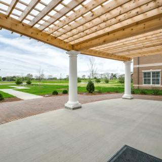 A covered patio with a pergola and columns overlooking a landscaped lawn and walkway.
