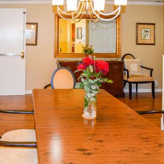 A cozy dining room featuring a wooden table with chairs, a chandelier, and a vase of flowers as a centerpiece.