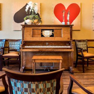 A cozy room featuring a vintage piano, surrounded by artwork and comfortable chairs.
