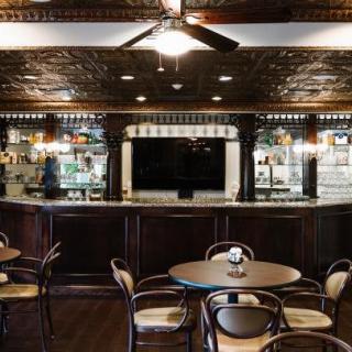A cozy bar interior with round tables and chairs, featuring a large television and classic decor.