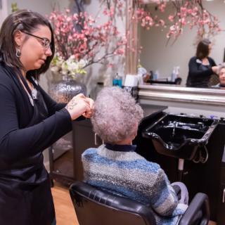 A hairdresser styles an elderly woman's hair in a salon setting.
