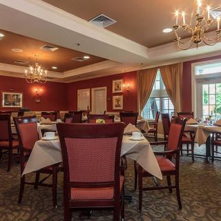 An elegantly decorated dining room with neatly arranged tables and chairs, adorned with chandeliers and curtains.