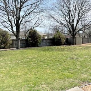 A grassy yard with trees and a fence on a clear day.