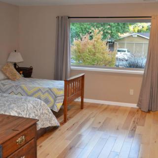 A cozy bedroom with a large window, wooden floor, and simple furnishings.