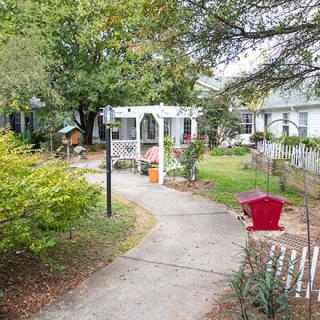 A serene garden pathway featuring a white pergola surrounded by lush greenery.